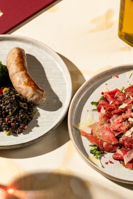 Carpaccio di manzo – plátky hovězí svíčkové s rukolou, citrónovou majonézou a růžovým pepřem – a Salsiccia fresca s černou čočkou a kadeřávkem, víno Barolo Giovanni Rosso 2021, toskánská restaurace Amiata Praha